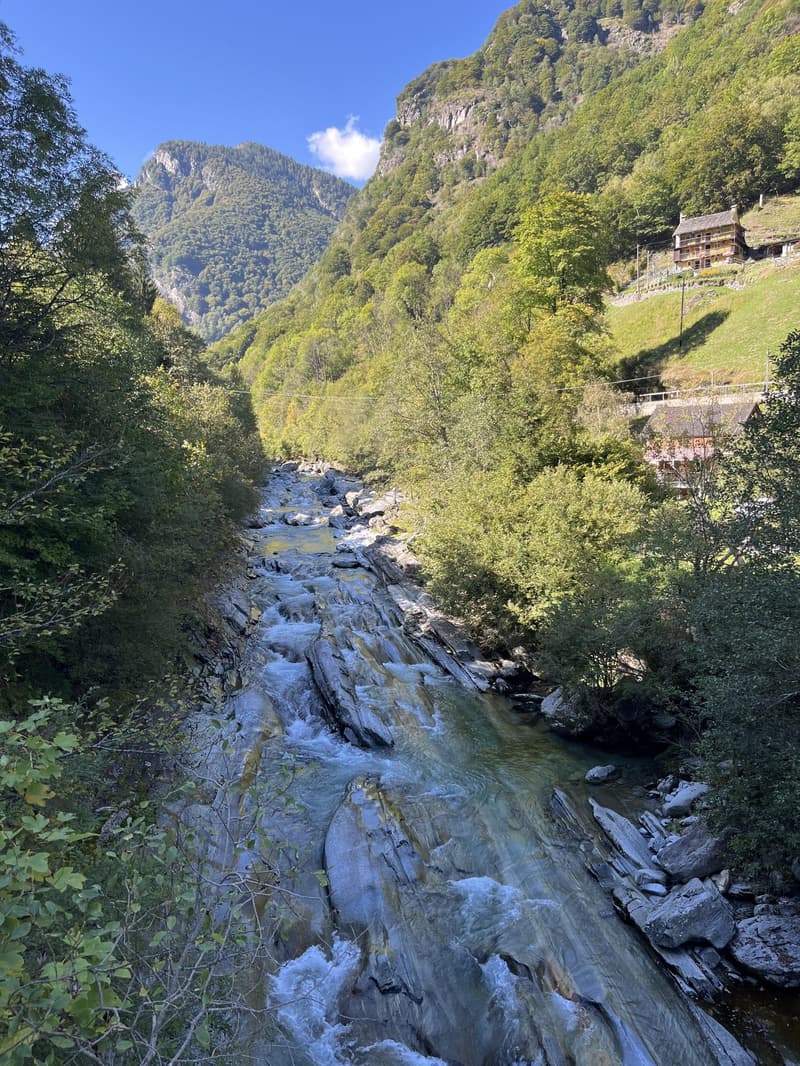 River flowing through a valley, surrounded by trees and rocks, with a house in the distance