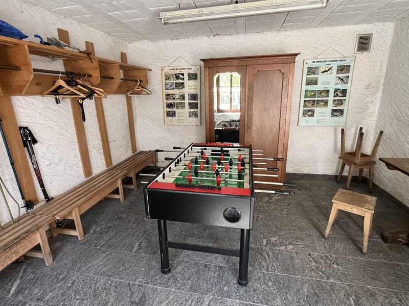 A room with a foosball table, wooden benches, a wooden cabinet, and a poster on the wall.