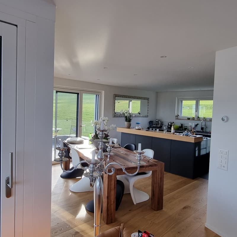 Open-plan dining and kitchen area with a table, chairs, mirror, and a view of the green field