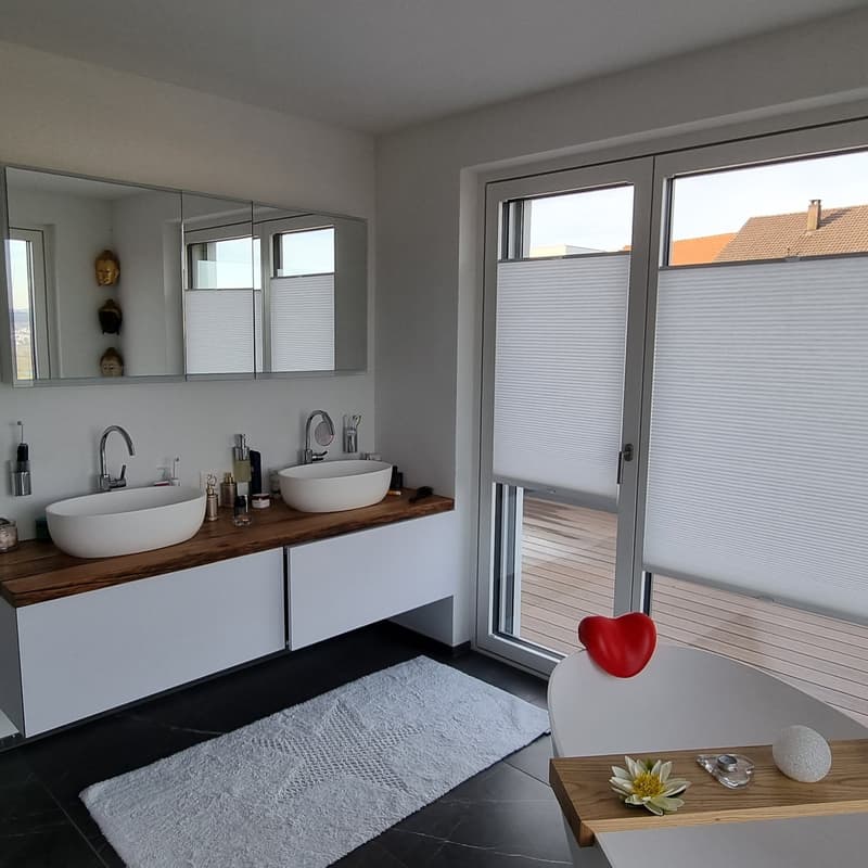 White double sink with wooden counter top, white walls, wooden floor, large mirror, window with wooden balcony, bathtub on opposite side