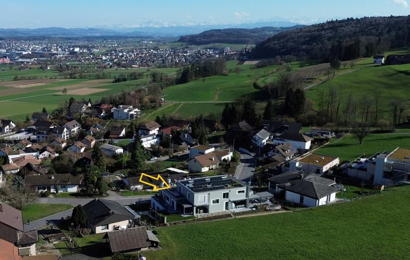 Detached house with solar panels on the roof, located in a rural area, surrounded by fields and mountains
