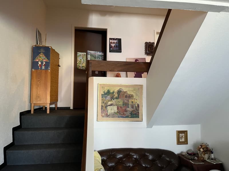 staircase, wooden cabinet, brown leather couch, picture frames, side table with flowers