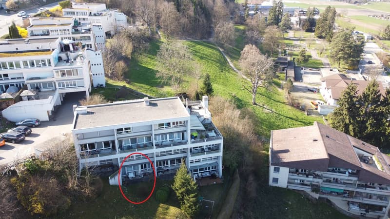 Aerial view of a white apartment building with multiple floors, balconies, and a red circle highlighting a specific area.