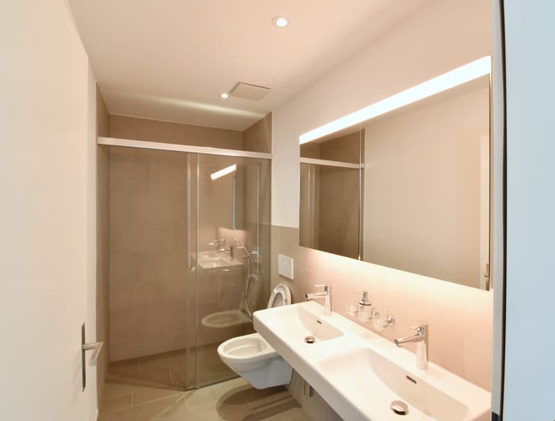 modern bathroom with glass shower, double sink, toilet, mirror, beige tiles, white walls