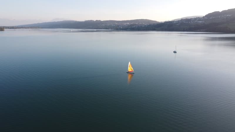 Aerial view of a lake with two sailboats, mountains in the background, and a clear sky.