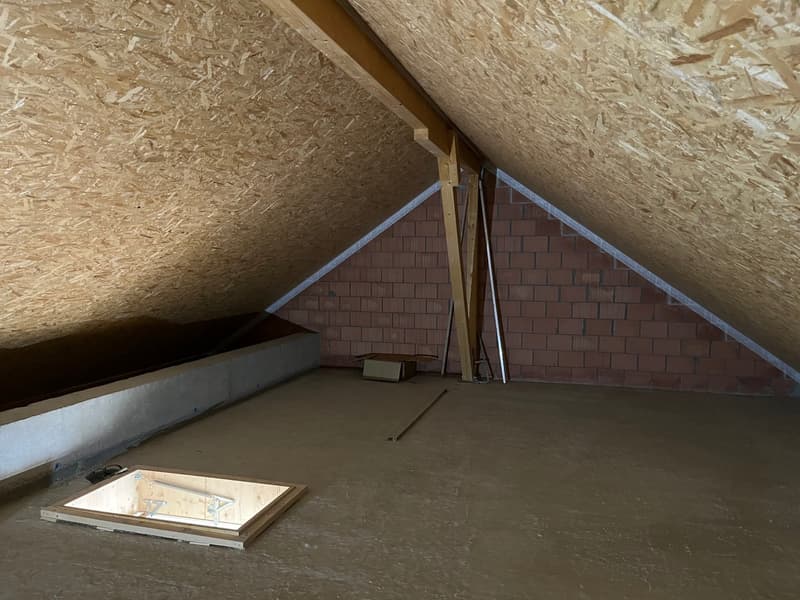unfinished attic room with wooden beams, brick wall, wooden floor, and a window