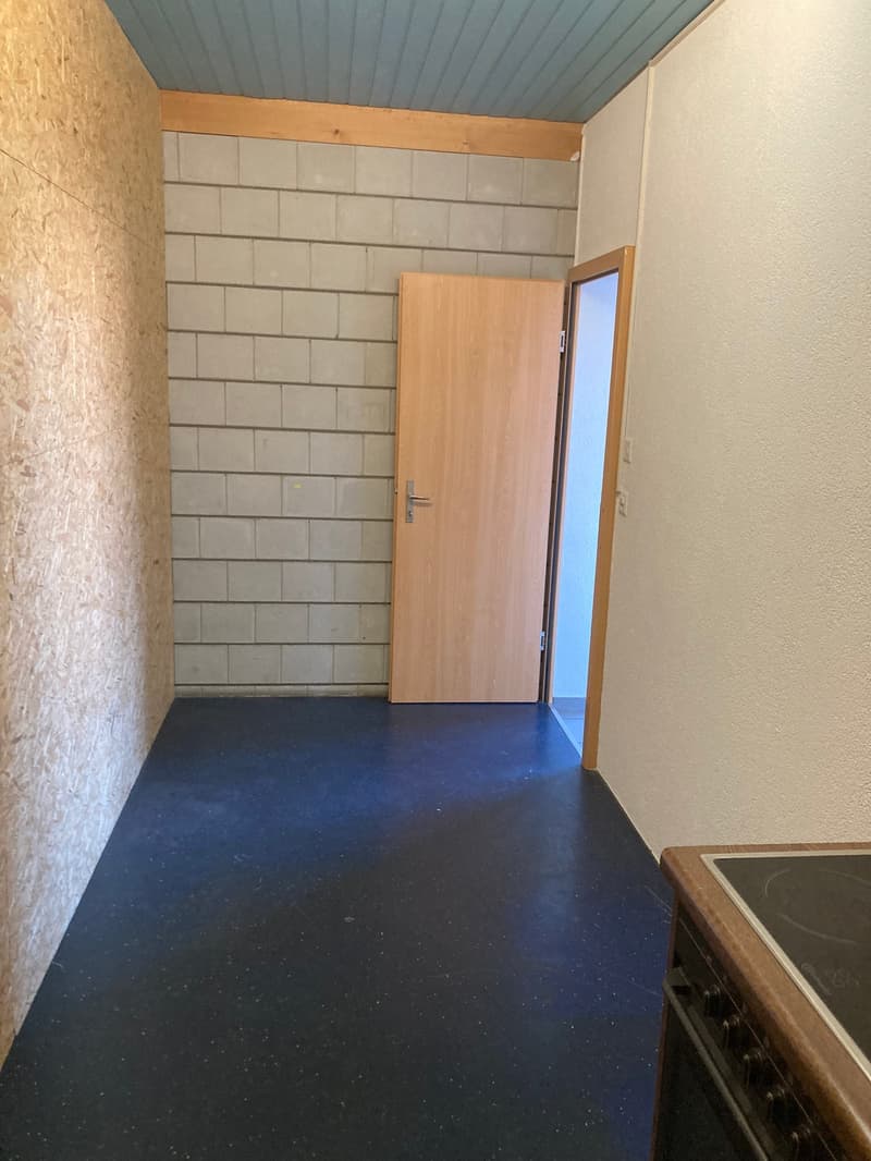 Empty room, brick wall, blue floor, wooden door, open door leading to another room, kitchen appliances.