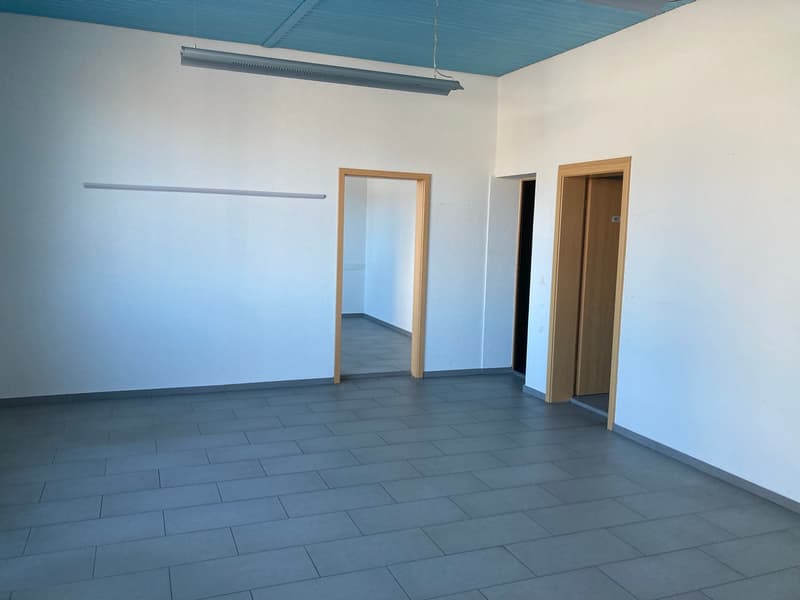Empty room, grey tiled floor, white walls, two doors, ceiling lamps
