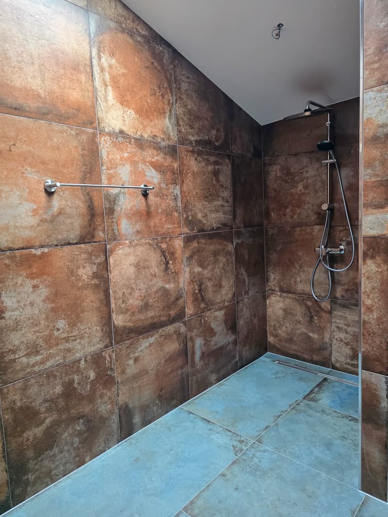 shower area with brown tiles, blue floor, shower head, and a towel rack