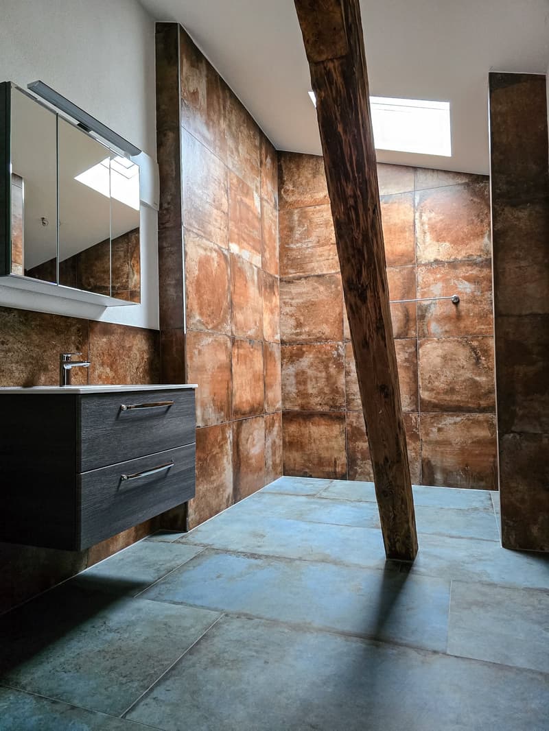 Bathroom with brown tiles, wooden pillar, mirror, sink, and faucet