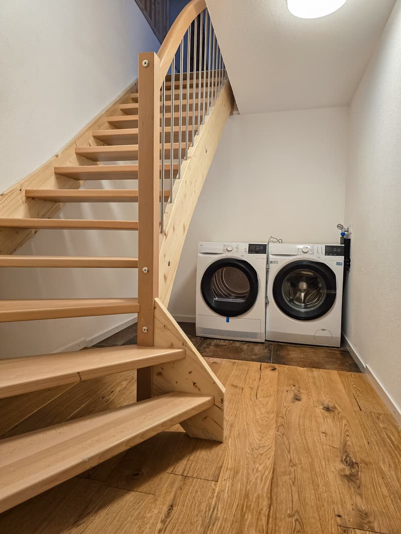 wooden stairs, white walls, wooden floor, two washing machines, one dryer
