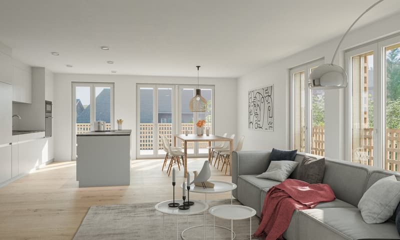 Spacious open-concept living room and kitchen with large windows, hardwood floors, modern gray sofa, dining table, and kitchen island. The room has a bright and airy feel with a balcony or terrace visible through the windows.