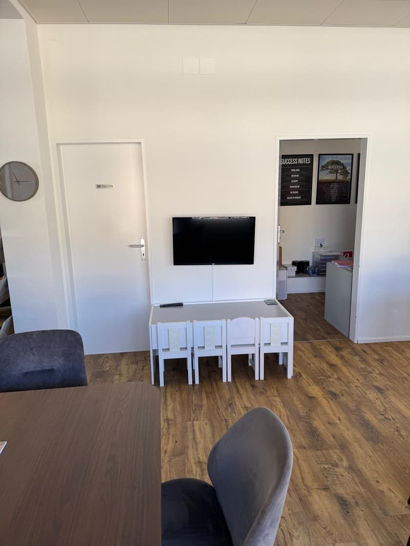 small room with a table, chairs, a television, and a door