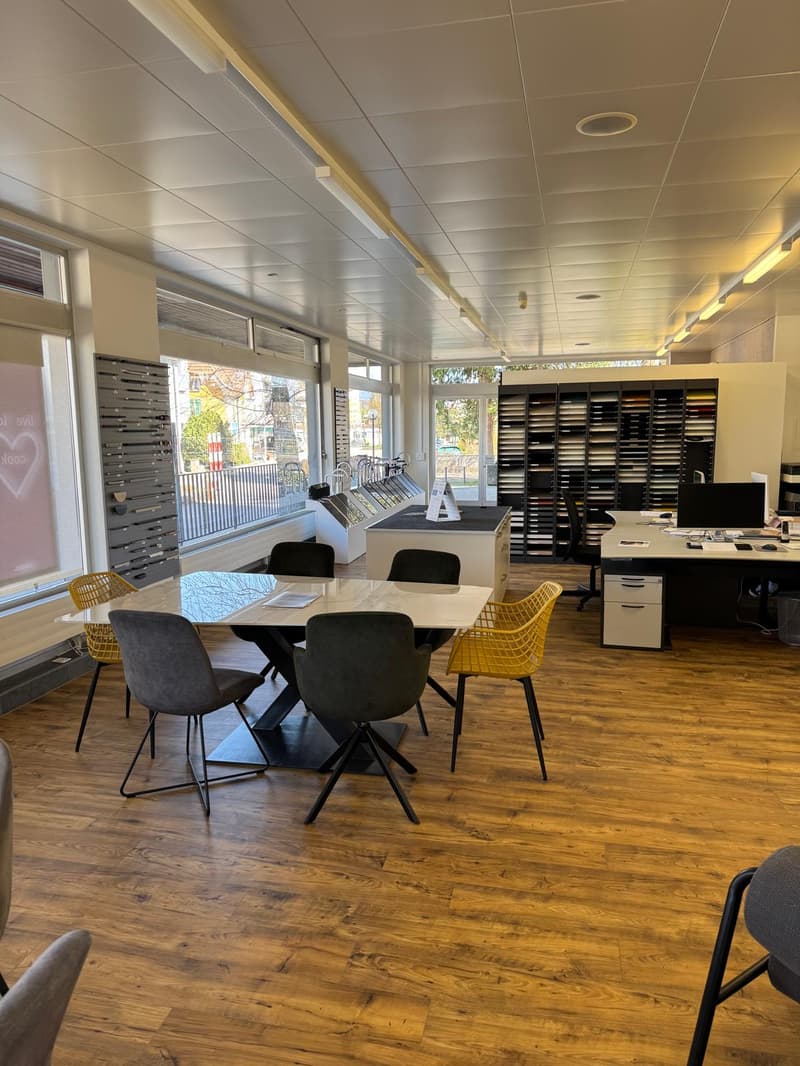 modern office with wooden floor, large windows, desks, chairs, computer monitors, shelves with various items