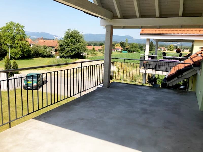 covered balcony with metal railings, concrete floor, view of a green field and mountains