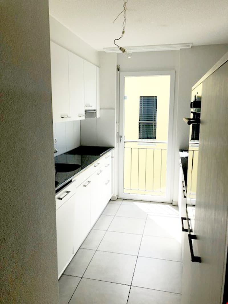 modern kitchen with white cabinets, black countertops, white tiles, glass door to balcony
