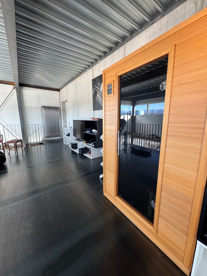 large open space, black floor, wooden sauna, white shelves, metal railing, radiator, black TV