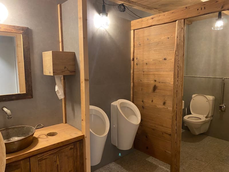 A bathroom with a wooden wall, a sink, two urinals, a toilet, and a mirror.