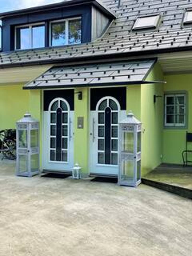 2 story house, yellow exterior, gray roof, two arched doors, parking area, lanterns