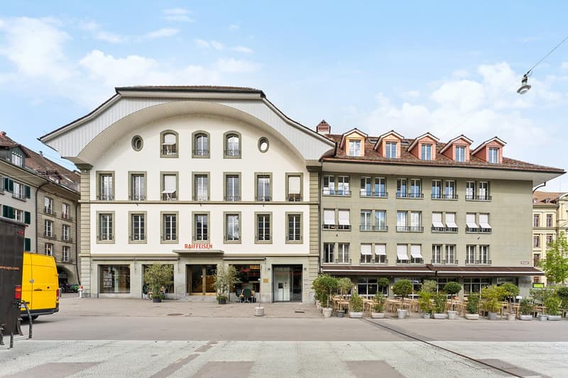 Corner house, 5 story, windows with shutters, outdoor patio area, Raiffeisen sign