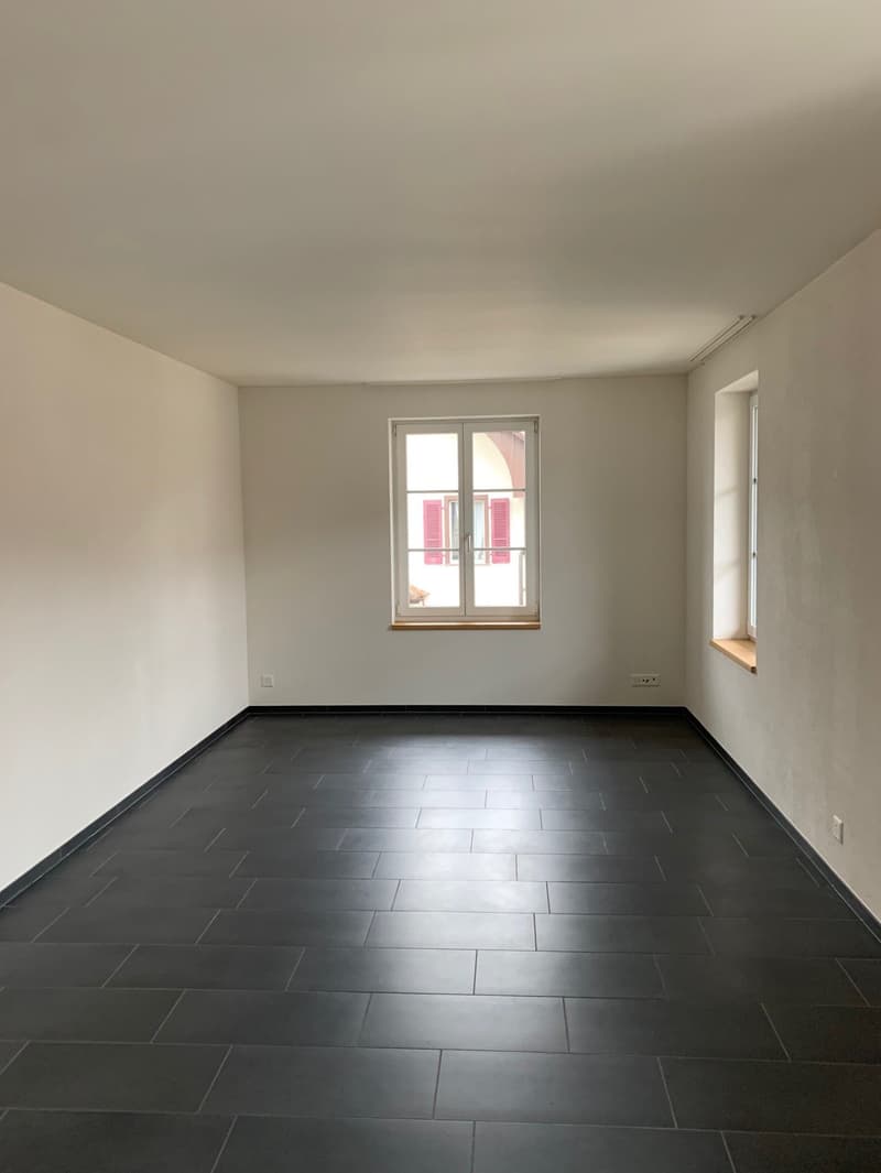 Empty room, black tile flooring, white walls, two windows, outlets on the wall