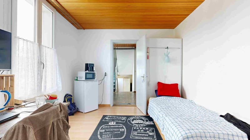 small room with bed, microwave, refrigerator, desk, chair, and window