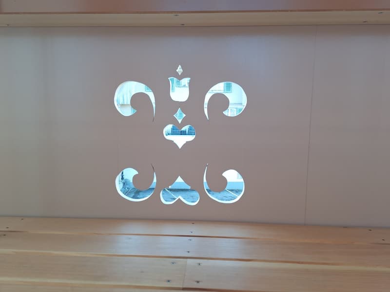 White wall with a unique fleur-de-lis cut-out design, wooden bench below