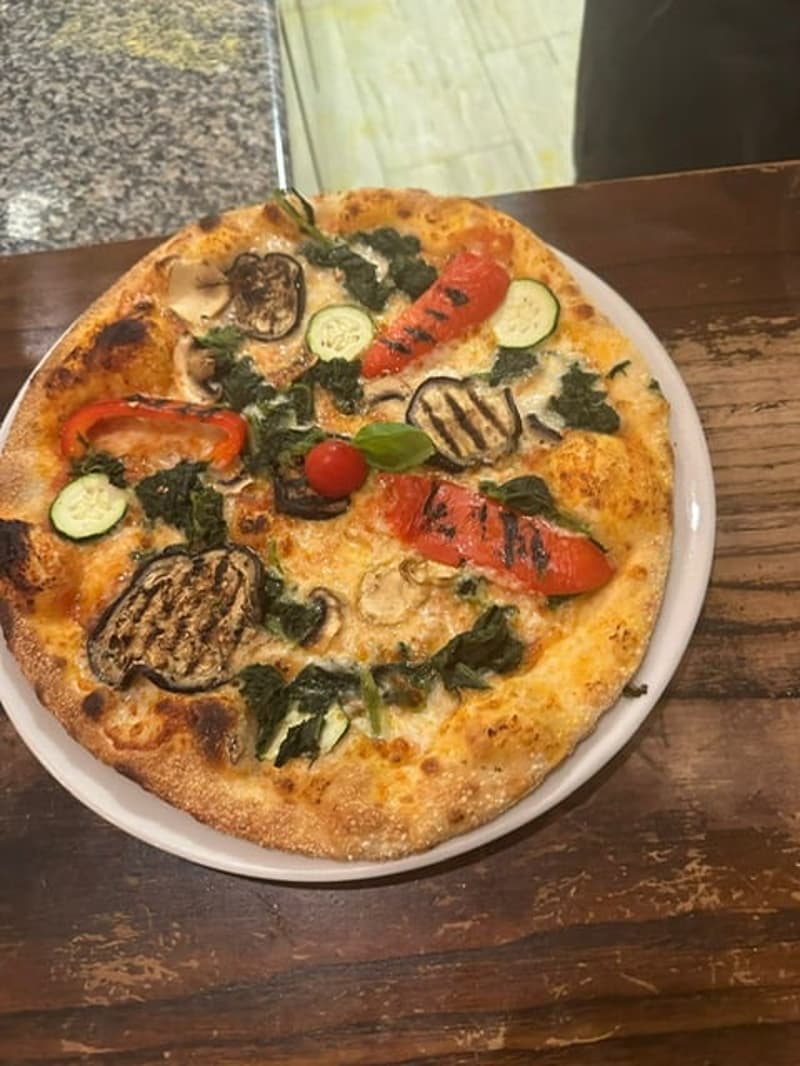 whole pizza on a white plate with vegetables on top