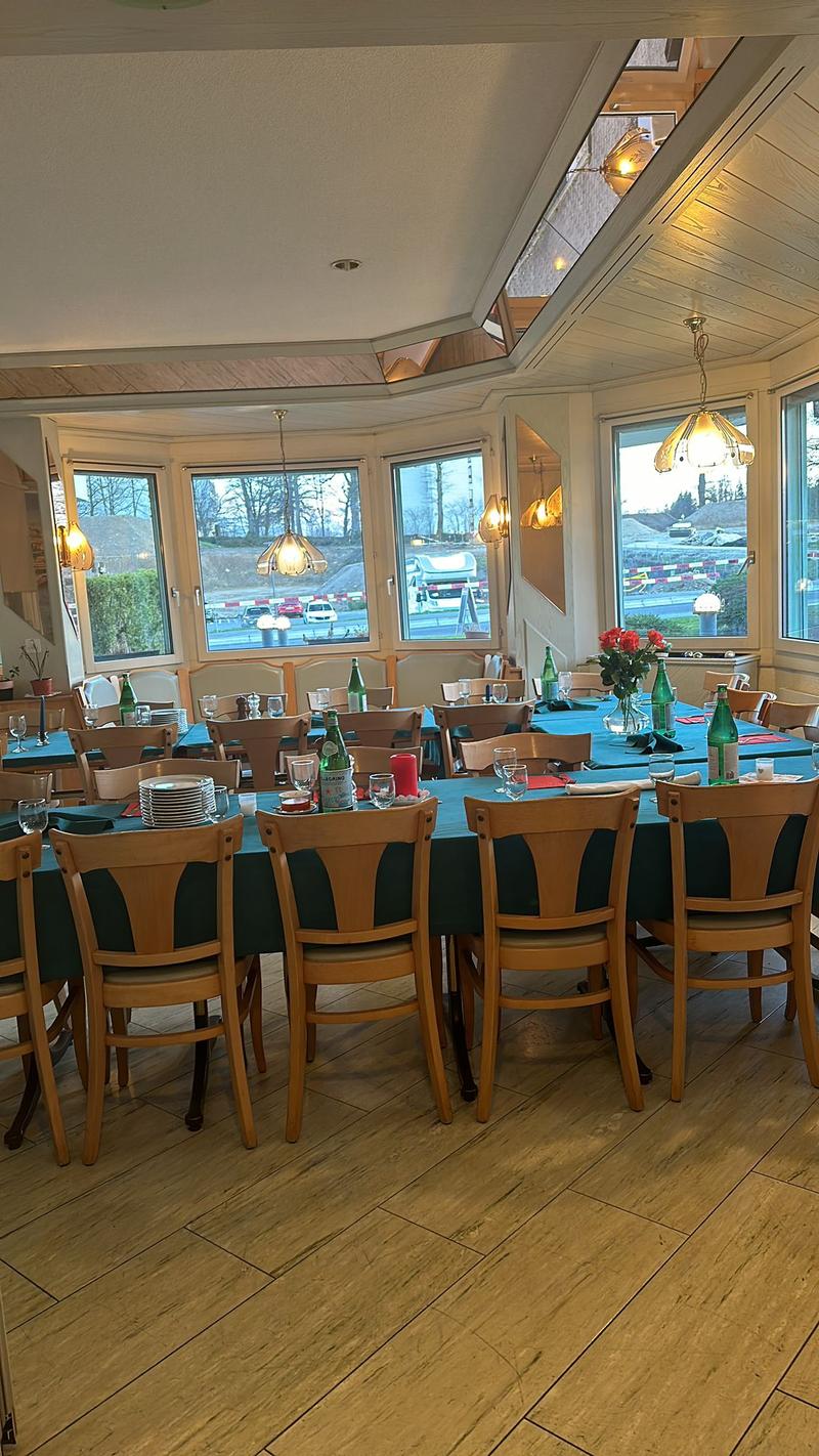 long dining table, wooden chairs, blue table cloth, wine glasses, plates, flowers, glass windows, lamps