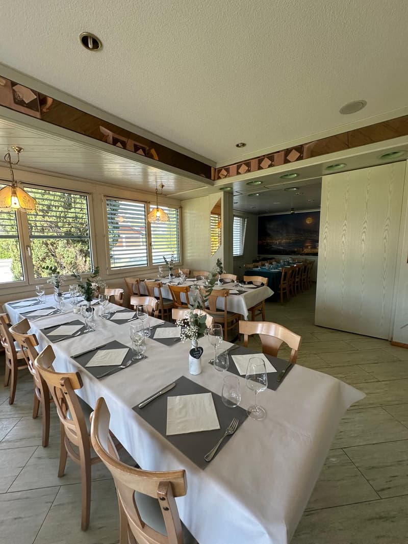 Dining area, white tablecloth, wooden chairs, long table, chandeliers, large windows, white floor, paintings, view