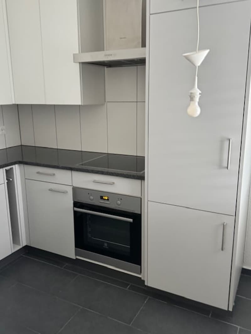 The image shows a modern kitchen with white cabinets, black countertops, and a built-in oven and dishwasher.