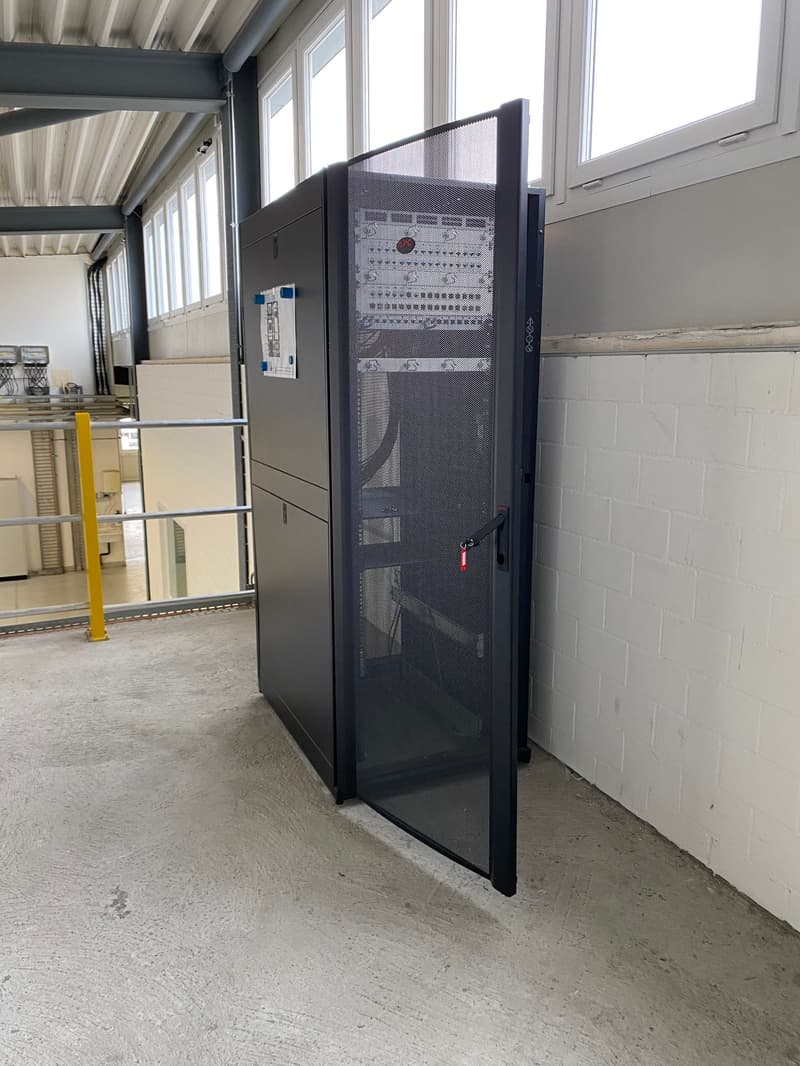 black metal server cabinet against the wall, white brick walls, windows with metal frames, grey concrete floor