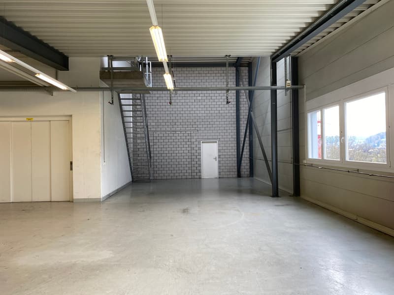 Industrial space with concrete floor, white walls, large windows, staircase, and metal beams