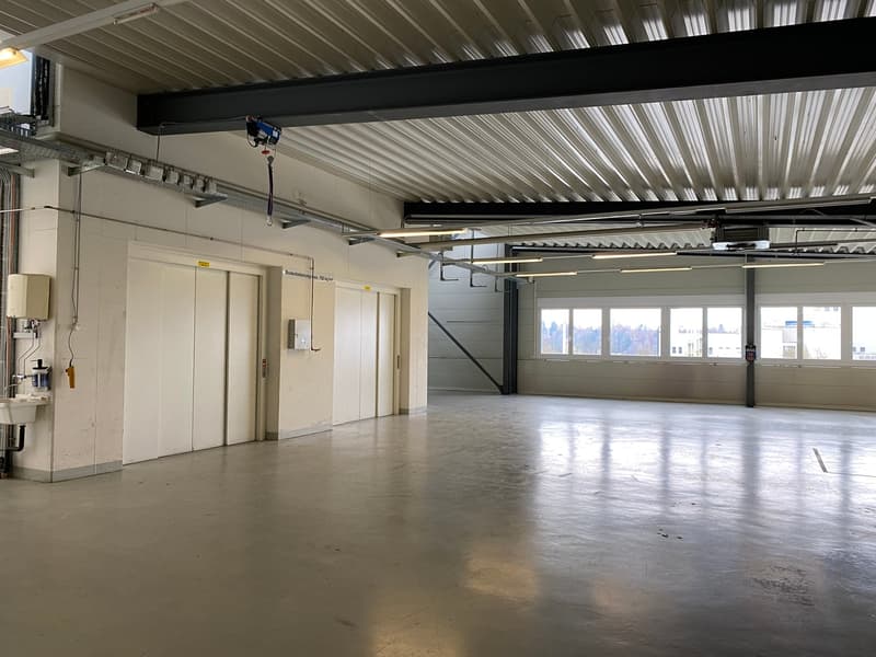 spacious warehouse, high ceilings, double doors, concrete flooring, bright fluorescent lighting, industrial shelving, industrial ventilation, windows
