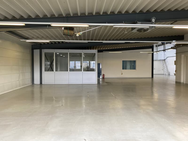 empty warehouse, fluorescent ceiling lights, metal ceiling beams, concrete floor, glass doors, a small fire extinguisher