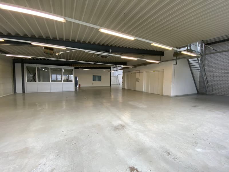 Industrial space with white walls and ceilings, concrete floor, fluorescent lighting, white doors, windows, and metal staircases.