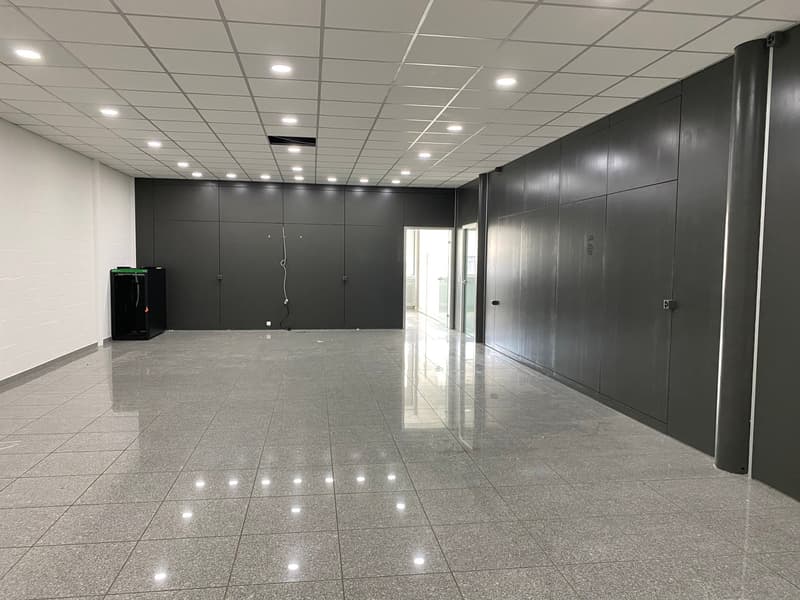 Empty room with gray tiled floor, white ceiling, gray walls, and a black object on the left side.