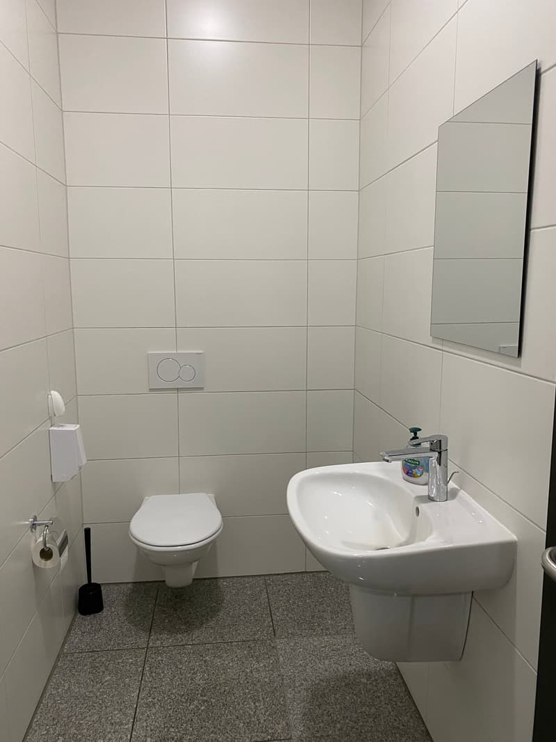 small bathroom with white tiles, white toilet, white sink, mirror, toilet paper, and soap dispenser