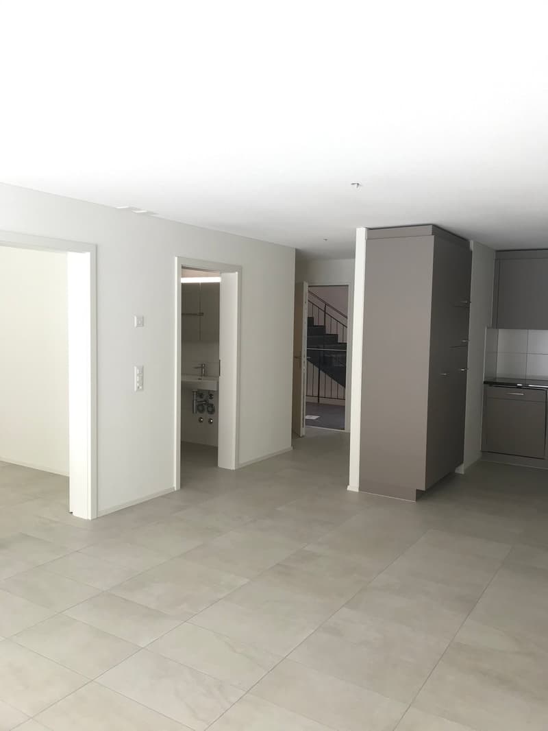 Empty room with white walls, tiled floor, open door, and a small sink in the corner