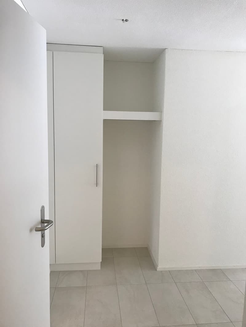 Empty room with white walls, white floor, and a white wardrobe with a hanging section and a shelf