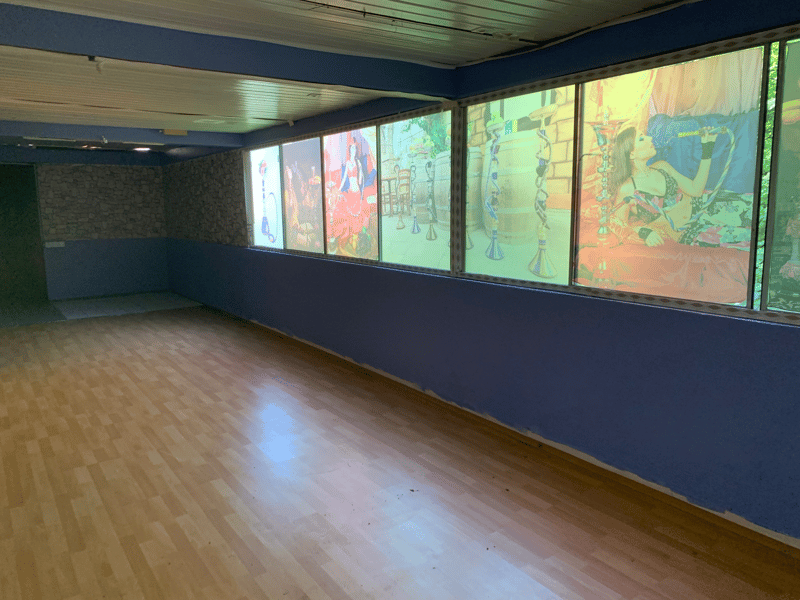 Large open room with hardwood floors, blue walls, and large windows displaying colorful artwork and murals.