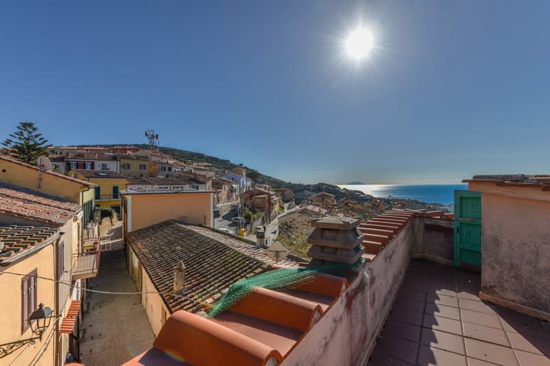 Panoramic view of a coastal town with colorful buildings, terracotta roofs, and a scenic ocean view in the background under a bright, sunny sky.