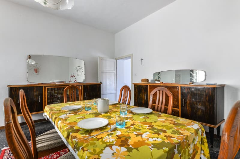Dining table with floral tablecloth, wooden chairs, wooden cabinets, mirrors on the wall