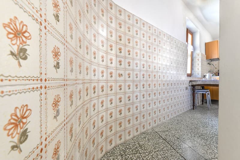 Patterned tile walls, terrazzo flooring, kitchen appliances and furniture visible in the background