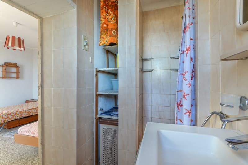Tiled bathroom with shelving unit, shower curtain, and a washing machine visible
