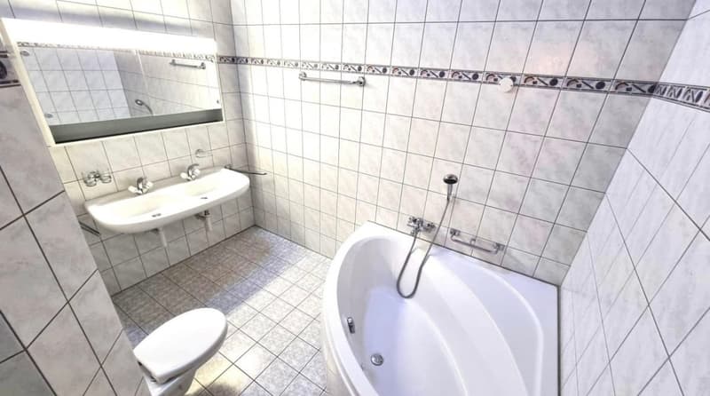 Tiled bathroom with a sink, toilet, and bathtub. The bathroom appears to have a private washing machine installed.