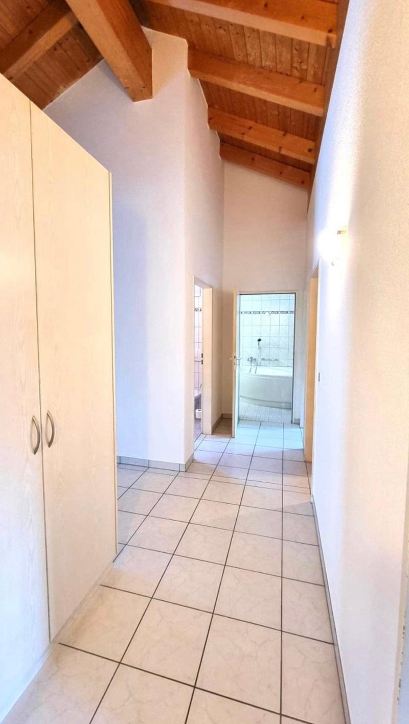 The image shows a hallway with a tiled floor and wooden ceiling beams. There is a closet or cabinet on the left side of the hallway, and a doorway leading to what appears to be a bathroom on the right side.