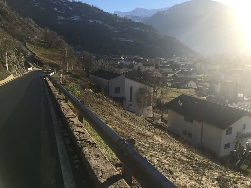 a road with a road side barrier going through a mountain, town view at the end