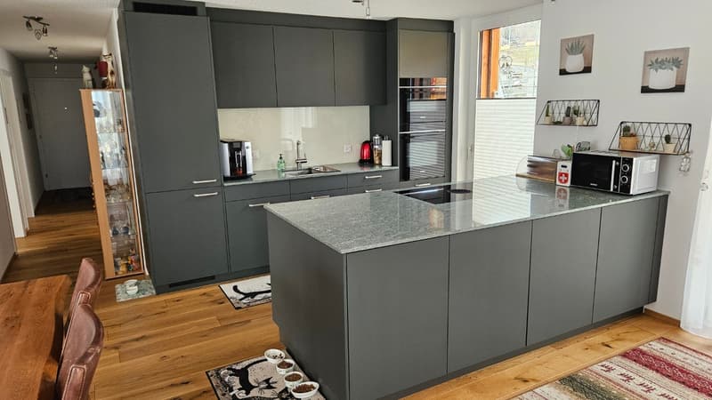 modern kitchen with island, granite countertop, built-in appliances, wooden floor, gray cabinets, white walls, decorative items