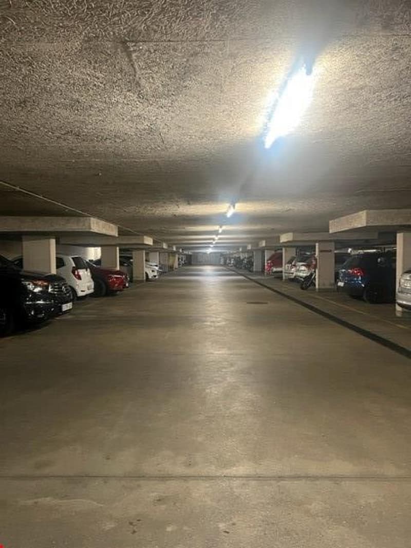 Well lit parking lot with multiple parked cars, concrete floor, pillars, and lights